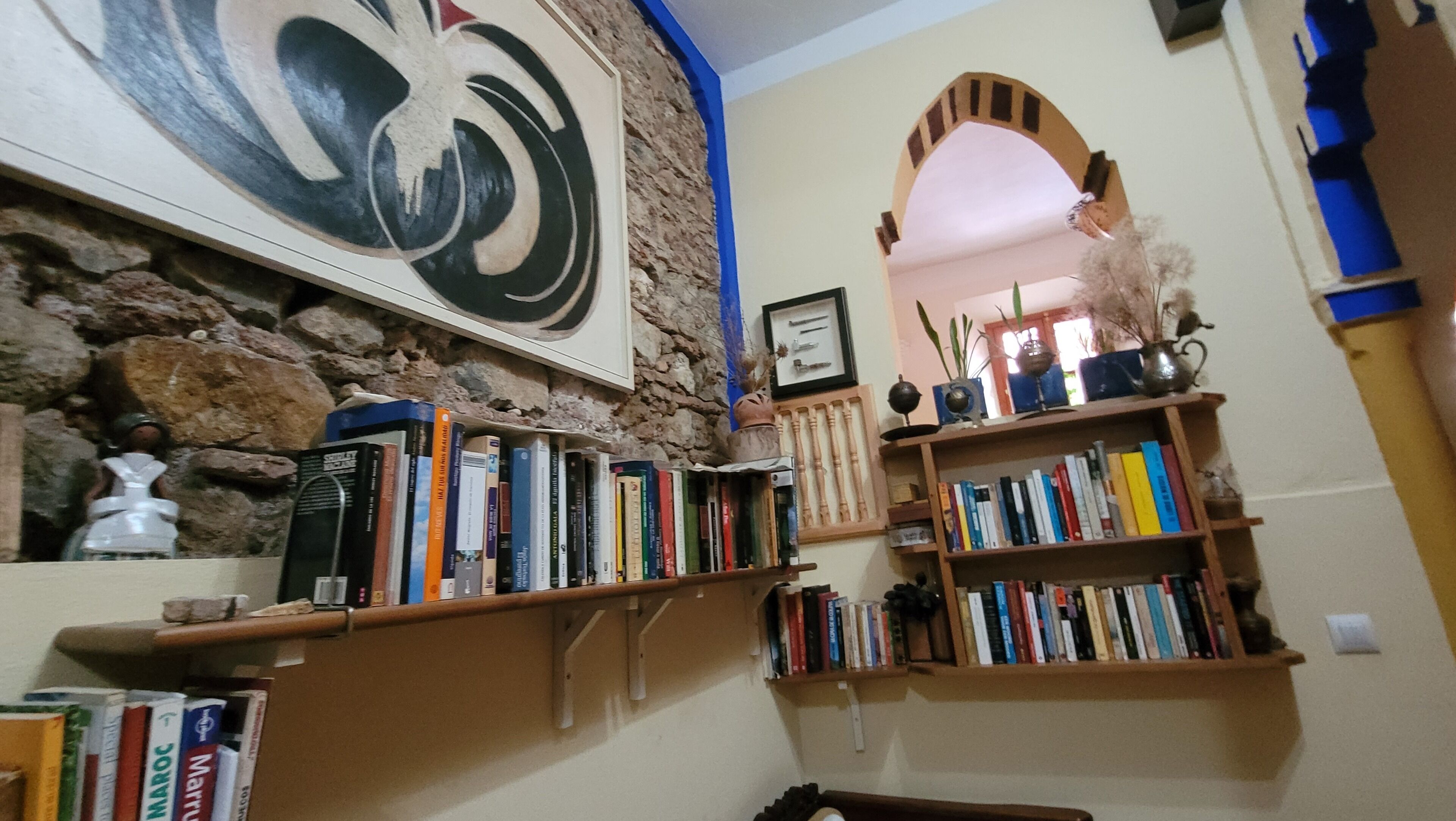 Um quarto com parede de pedra, uma grande pintura abstrata e estantes cheias de livros.