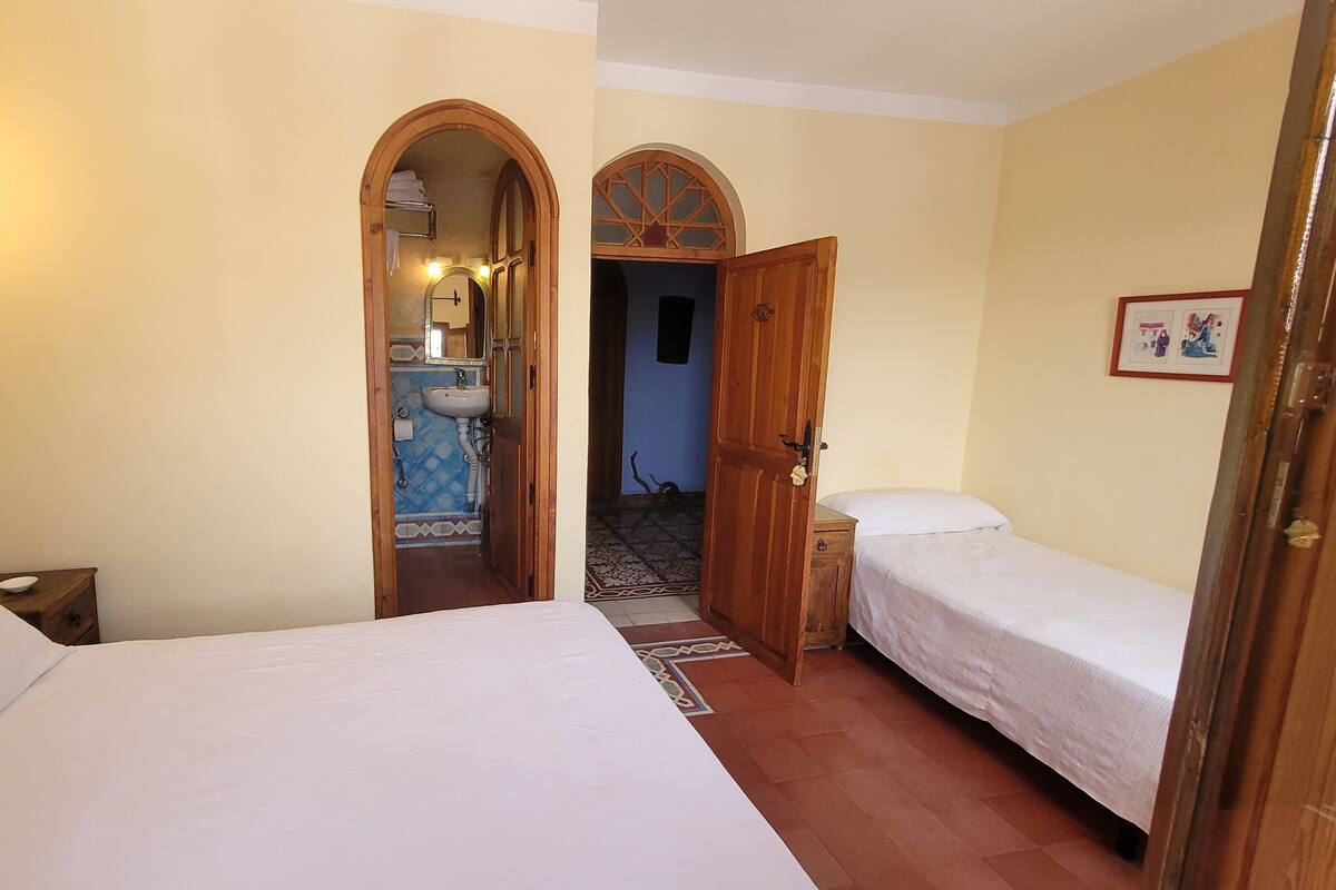 A room with two beds, a bathroom with a sink, and a door leading to another room.