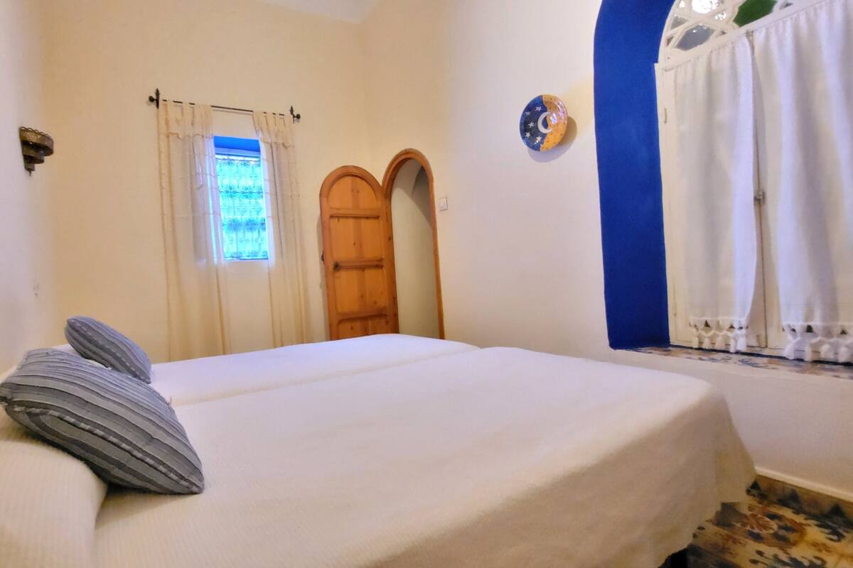 A bedroom with a bed, a window with curtains, a door, and a wall with a decorative plate.
