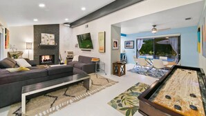 A modern living room with a sofa, fireplace, and a poolside area with a table and chairs. - The Colony Enclave - #1 Hideaway in Palm Springs (Palm Springs)