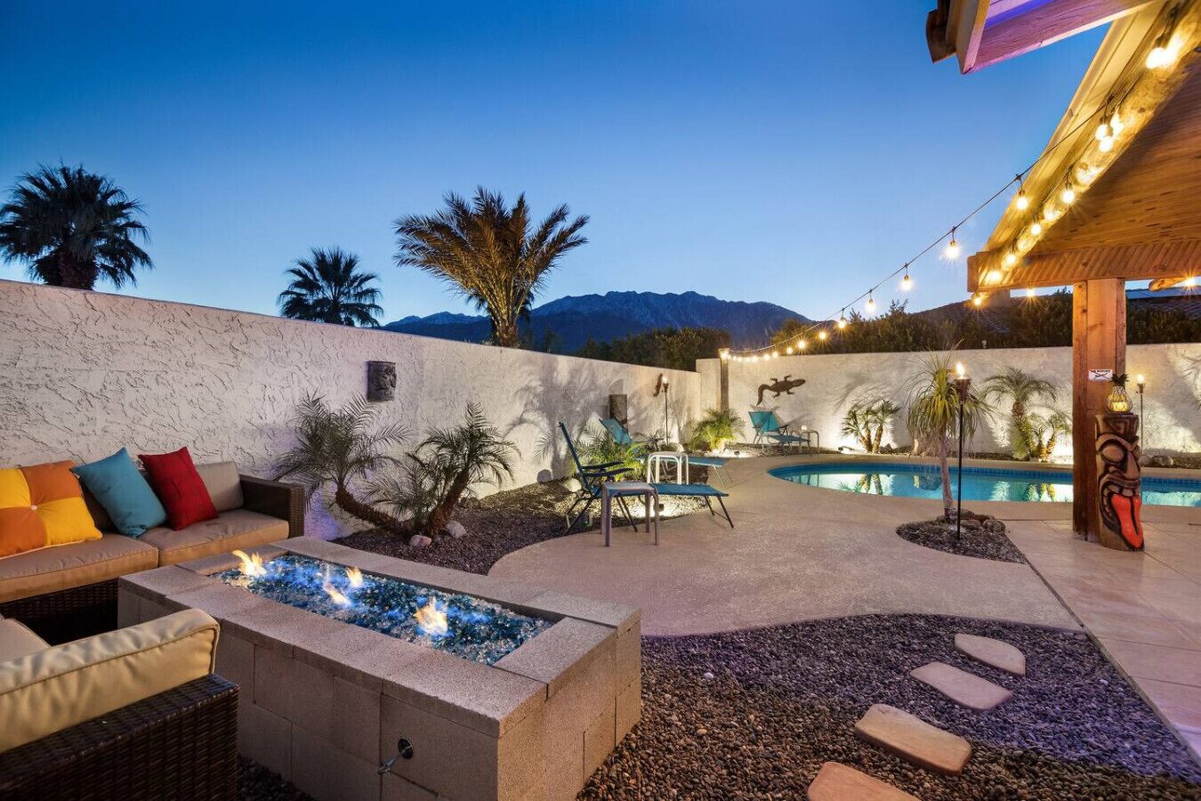 A backyard with a fire pit, outdoor seating, a pool, and string lights.
