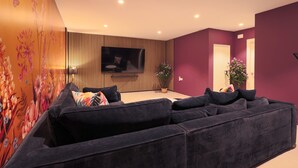 A modern living room with a sectional sofa, a flat-screen TV, and a floral wall mural.