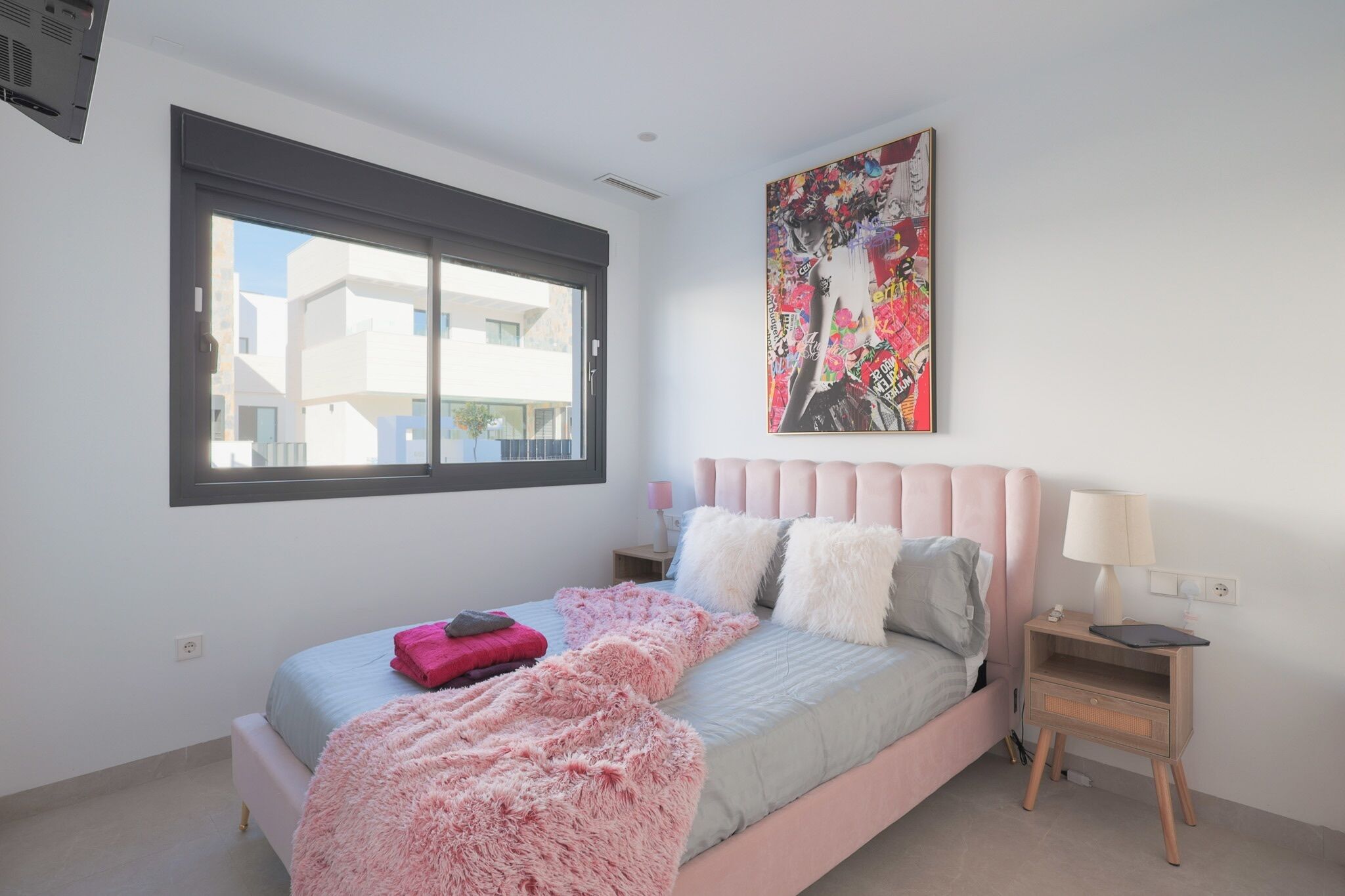 A bedroom with a bed, a nightstand, a window, and a painting on the wall.