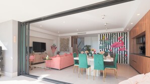A modern living room with a pink sofa, green chairs, and a dining area with a white table.