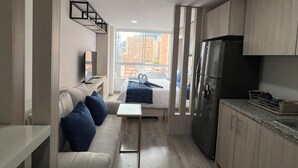 Ett modernt kök med ett inbyggt kylskåp, en matplats med soffa och stolar samt ett stort fönster med utsikt över omgivande byggnader.