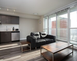A modern living room with a black leather sofa, a wooden coffee table, and a kitchen area with a dishwasher and cabinets. - Chic 1BR Apt with Rooftop Patio near Jasper Avenue (Edmonton)