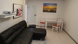 A modern living room with a black leather sofa, a white dining table with two chairs, a projector on a shelf, and a painting of sunflowers. - Vacation home with summer pool and garage, free of stairs/steps (Jesewitz)