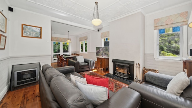 A spacious living room with a fireplace, leather sofas, and a dining area with natural light. - Ferntree Cottage in Blackheath (Blackheath)