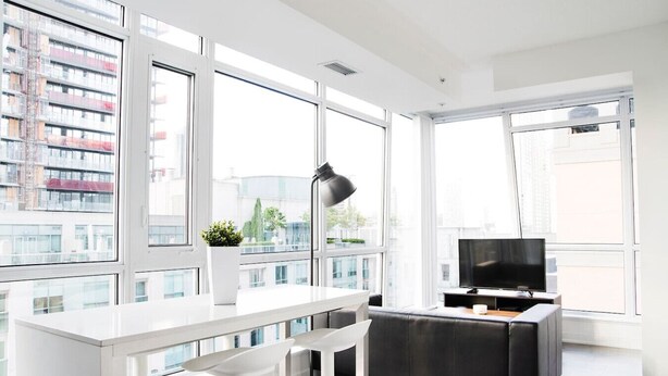 A modern living room with large windows, a white sofa, a black TV stand, and a small table with a plant.