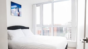 A modern bedroom with a large window, a bed with white linens, and a city view.