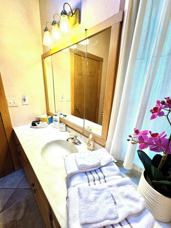 A bathroom with a wooden vanity, a large mirror, and a sink. There are towels and toiletries on the vanity. - Paradise in Forest setting w/ Ocean views, hot tub, close to town & Hiking (Eastsound)