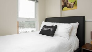 Una cama con ropa blanca, un cabecero negro y una almohada con texto.
