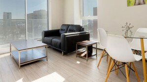 Una sala moderna con un sofá de cuero negro, una mesa de centro de vidrio y un comedor con sillas blancas y una mesa de vidrio.