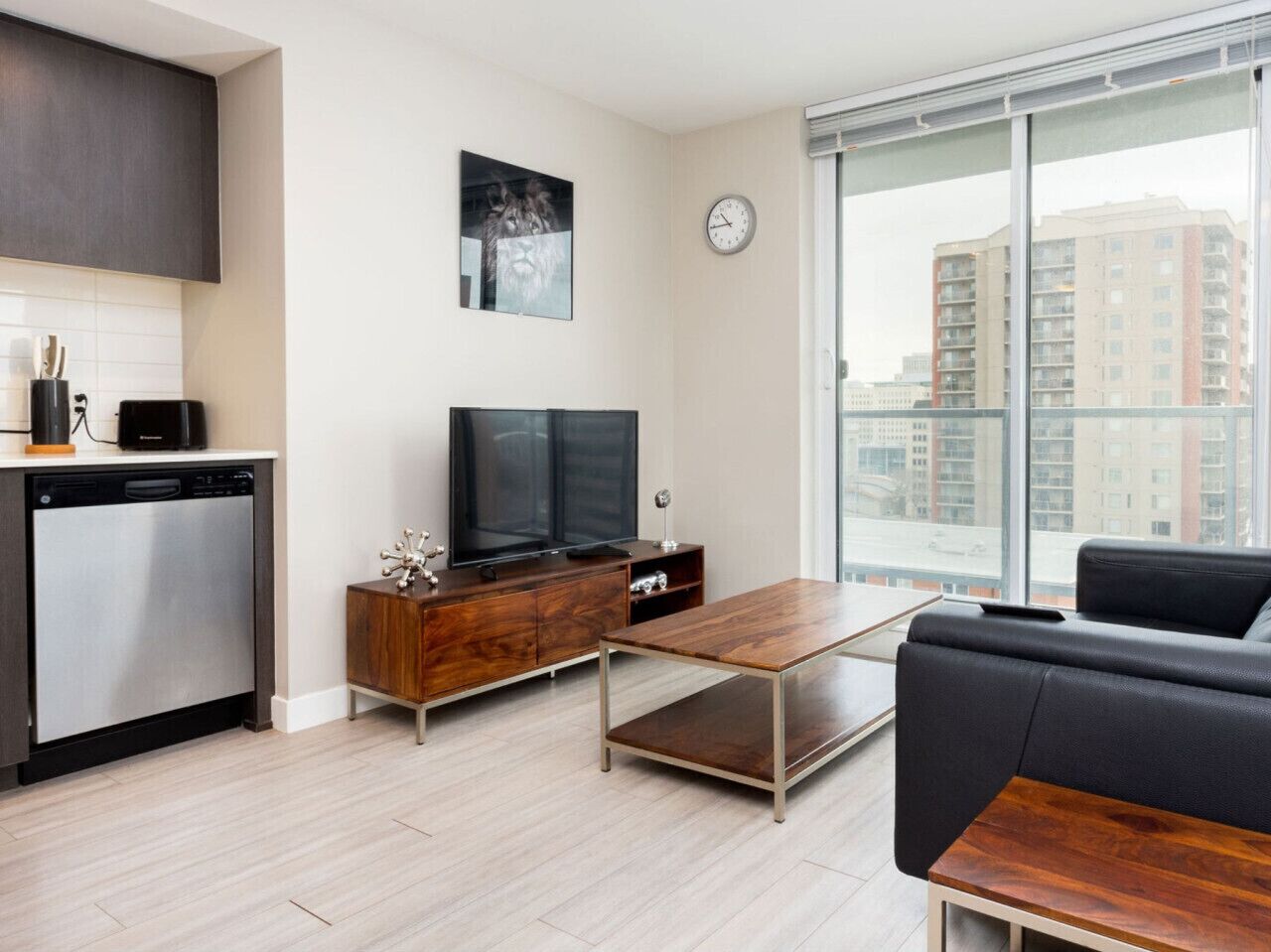 A modern living room with a flat-screen TV, wooden furniture, a sofa, and a large window with a city view.