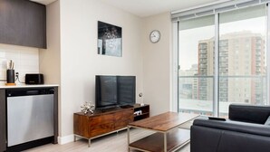 Una sala de estar moderna con televisor de pantalla plana, muebles de madera, un sofá y un ventanal con vistas a la ciudad.