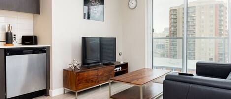 A modern living room with a flat-screen TV, wooden furniture, a sofa, and a large window with a city view.