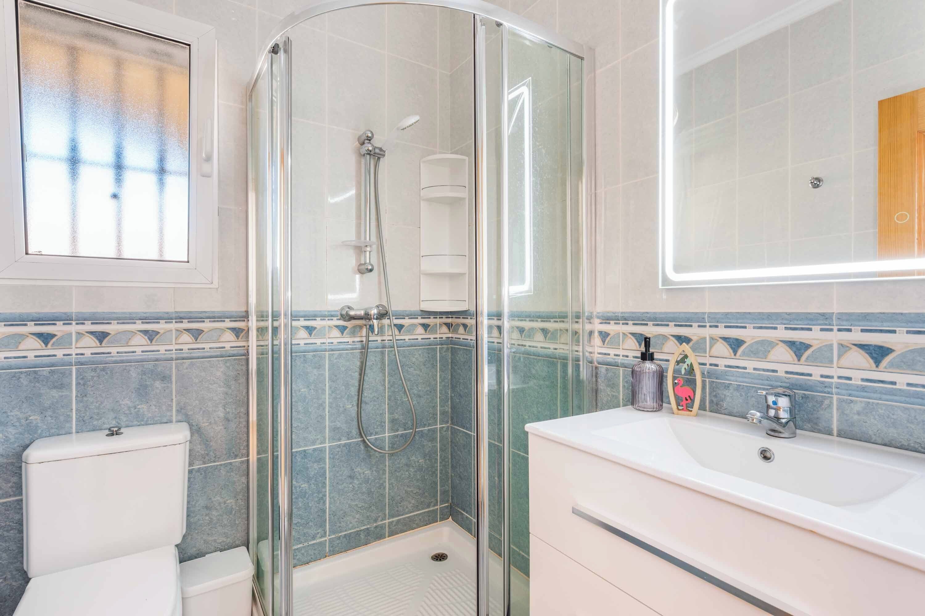 A bathroom with a glass-enclosed shower, a white sink, and a mirror.