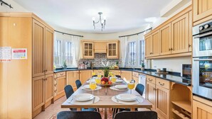 Una cocina moderna con armarios de madera, una isla central con fruta y bebidas, y un comedor con sillas y una mesa dispuesta para cuatro.