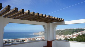 A balcony with a wooden pergola, a view of the sea, and a coastal town in the background. - Lar da Onda - By SCH (Nazaré)
