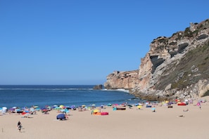 Uma praia com tendas e guarda-sóis, falésias rochosas e o oceano.