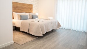 A neatly made bed with a wooden headboard, a fluffy beige rug, and a white curtain. - Lar da Onda - By SCH (Nazaré)