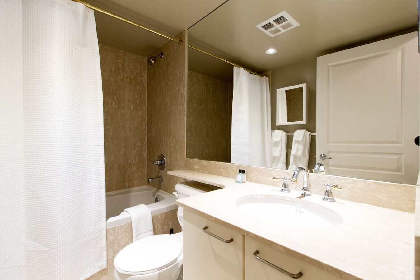 A bathroom with a bathtub, two sinks, a toilet, and a large mirror.