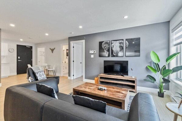 A modern living room with a grey sofa, a wooden coffee table, and a flat-screen TV.