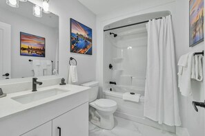A modern bathroom with a double sink, toilet, and shower. There are two framed pictures on the wall.