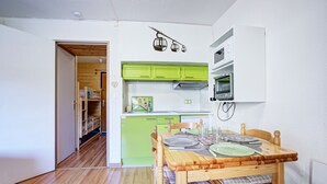 A compact kitchen with green cabinets, a dining table set with plates and glasses, and a microwave above the counter. - Le Petit Montagnard - Station accessible à pied (Les Angles)