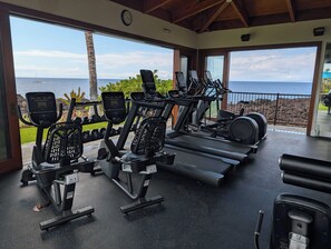 Academia com equipamentos de cardio e vista para o oceano.