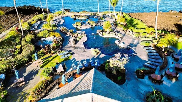 Vista aérea de un resort con piscina, zonas de descanso y palmeras.