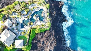 Vista aérea de un resort con varias piscinas, una zona de playa y un litoral rocoso.