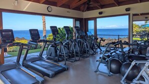 Un gimnasio con cintas de correr, elípticas y equipo de pesas, con vista a un paisaje marino.