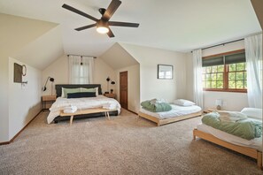 A bedroom with a sloped ceiling, a ceiling fan, two beds, a window with curtains, and a door.