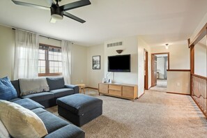 A living room with a sectional sofa, ottoman, TV, and a ceiling fan.