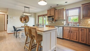 Una cucina moderna con mobili in legno, un'isola centrale, un'area pranzo con sedie e un'ampia finestra che offre luce naturale.