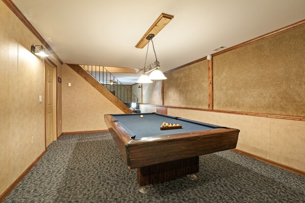 A pool table in a room with carpeted flooring, wooden walls, and a ceiling fan.