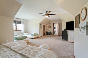 Um quarto espaçoso com uma cama grande, um ventilador de teto, uma janela com cortinas, uma escrivaninha com computador e uma cadeira.