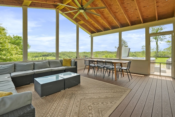 Uma área de estar coberta ao ar livre, com sofá, cadeiras e uma mesa, com vista para uma paisagem deslumbrante.