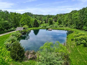 Ein ruhiger Teich, umgeben von üppigem Grün, einer Holzterrasse und einem kleinen Pavillon.