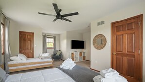 Una camera da letto con due letti, un ventilatore a soffitto, una TV e un'ampia porta in legno.