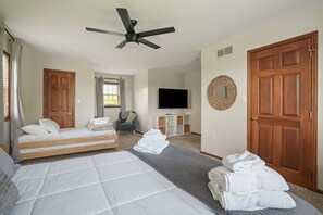 A bedroom with two beds, a ceiling fan, a TV, and a large wooden door.