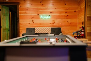 A pool table with a neon sign reading 'The Shagbar' in a room with wooden walls and a green door.
