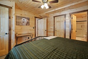 A wooden-paneled room with a bed, a ceiling fan, and a painting of an owl.