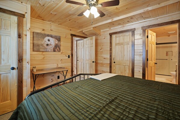 A wooden-paneled room with a bed, a ceiling fan, and a painting of an owl.