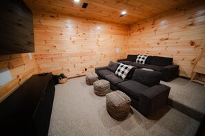 A cozy room with wooden walls, a dark sofa set, and a flat-screen TV.