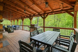Una terraza techada al aire libre con muebles de madera, una parrilla y vistas a un bosque.