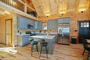 A spacious kitchen with wooden walls, a large island with stools, stainless steel appliances, and a mezzanine level.