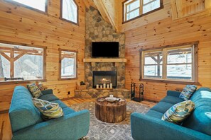 A cozy cabin interior with a stone fireplace, wooden walls, and blue sofas.