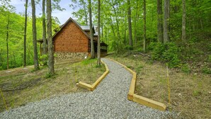 Una cabaña de madera rodeada de un bosque, con un camino de grava que conduce a ella.